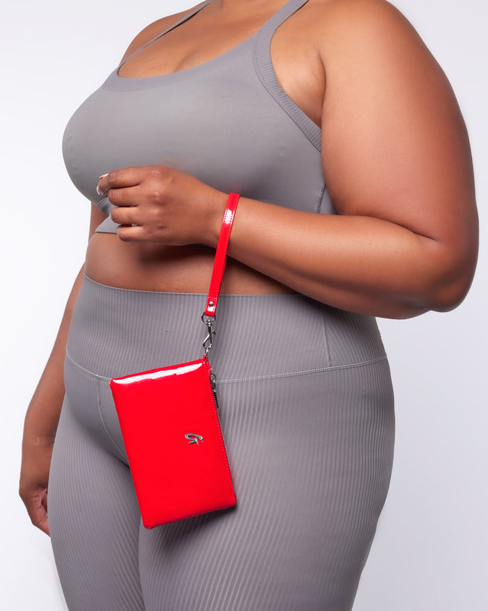 Mini silver wristlet with a mirror red finish, attached to a matching red strap, worn by a woman in gray activewear.