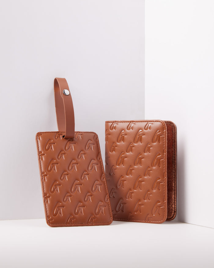 Brown monogram passport holder and luggage tag with embossed G pattern, made of leather, against a white background.