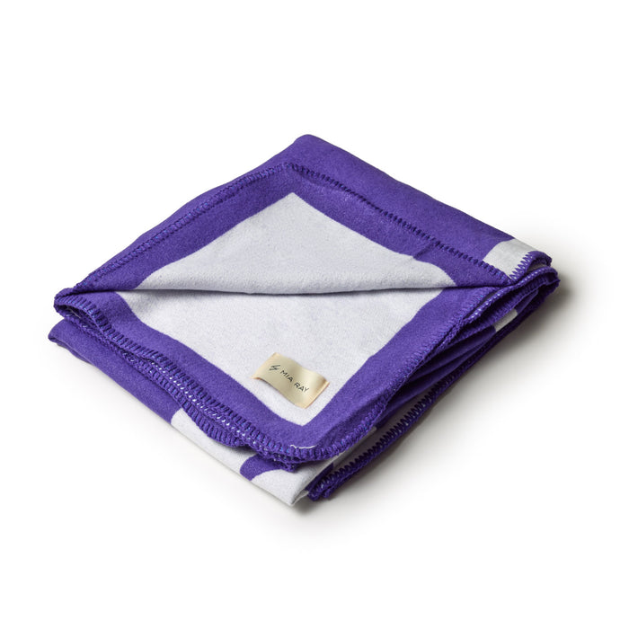 Purple classic throw blanket folded with a white and purple border, featuring a small beige label.