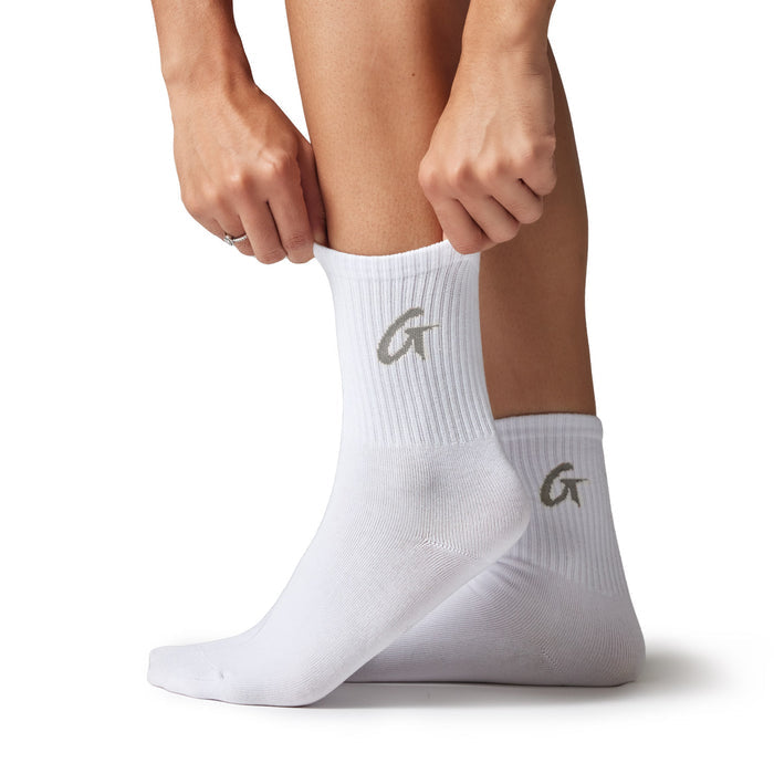 White crew socks with a gray "G" logo, ribbed texture, and mid-calf length, shown on a person adjusting the sock.