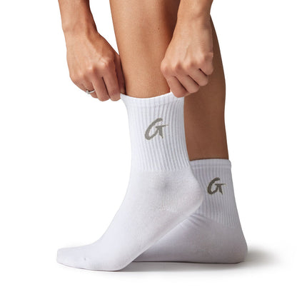 White crew socks with a gray "G" logo, ribbed texture, and mid-calf length, shown on a person adjusting the sock.