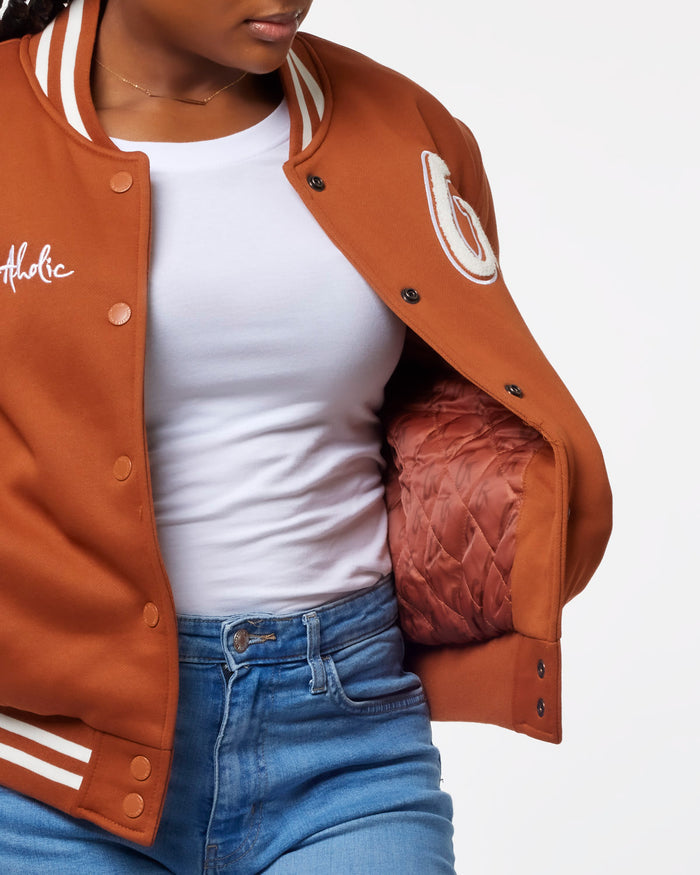 Brown essential varsity jacket featuring a quilted lining, styled with a white t-shirt and denim jeans.