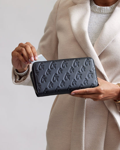 Black matte wallet with embossed monogram G pattern, shown with a person holding a card.