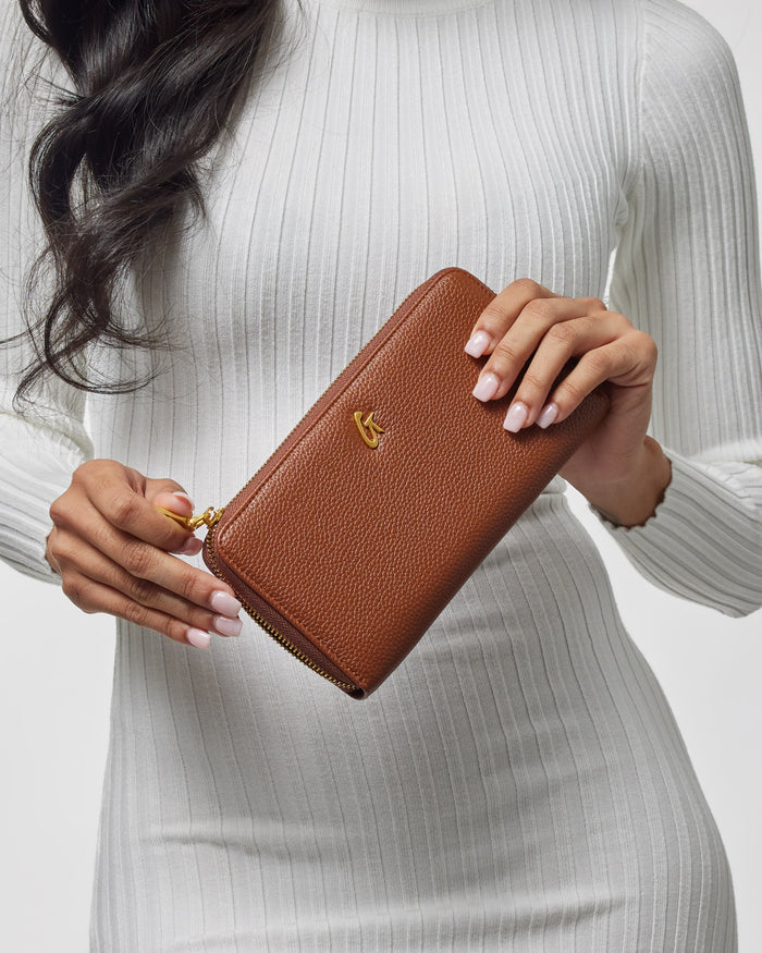 Brown jumbo pebble leather wallet with a gold logo, held by a woman in a white ribbed top.
