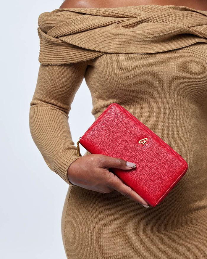 Red jumbo pebble leather wallet with a gold logo, held by a person in a beige sweater.