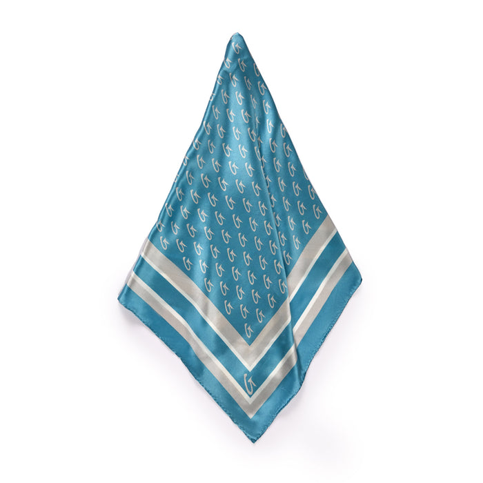 Large blue silk scarf with silver monogram pattern, border design, and a small logo in the corner.