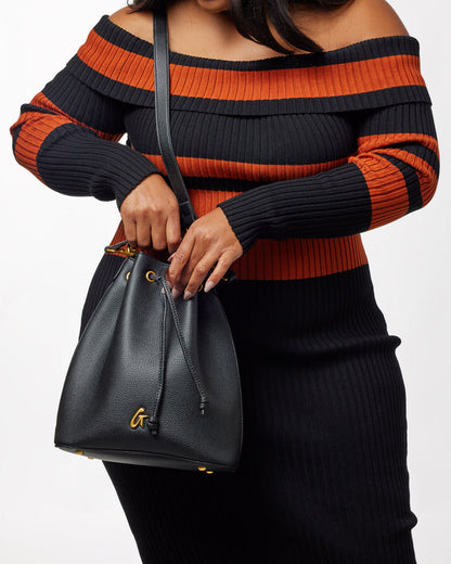 Black Pebble Bucket Bag bundle with gold accents, worn by a woman in a black and orange striped off-shoulder sweater.