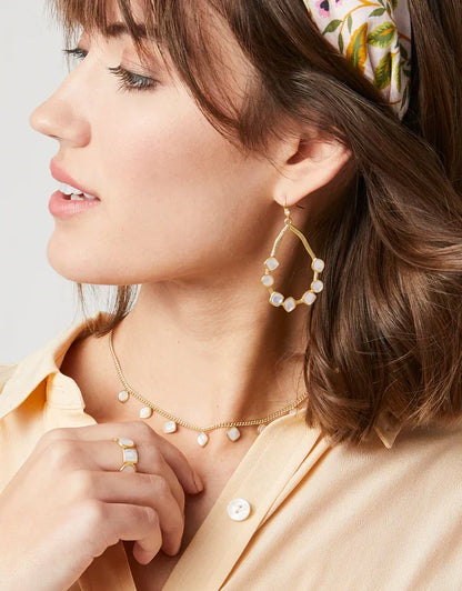 Woman wearing gold hoop earrings and a necklace with a neutral background