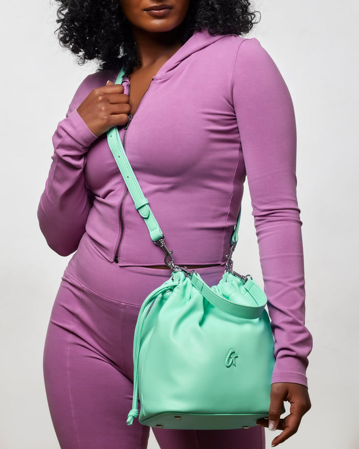 Teal medium drawstring bucket bag held by a woman in a purple outfit, showcasing a stylish and functional accessory.