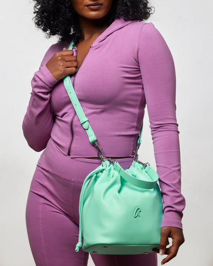Teal medium drawstring bucket bag held by a woman in a purple outfit, showcasing a stylish and functional accessory.