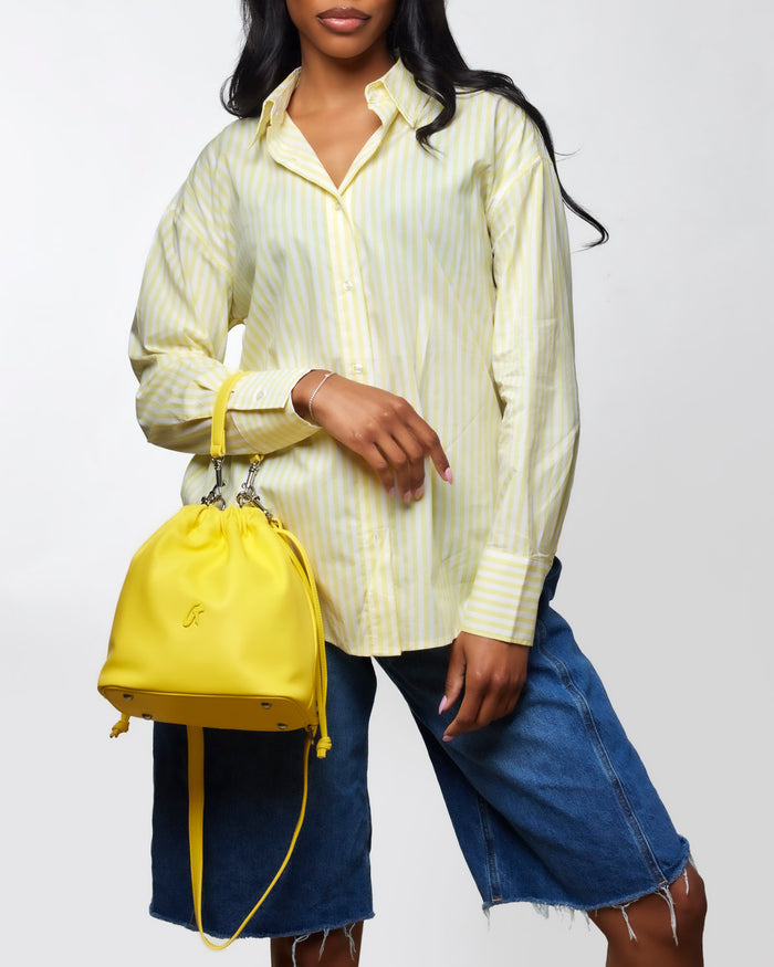 Medium yellow drawstring bucket bag held by a woman wearing a striped shirt and denim shorts, showcasing a stylish look.