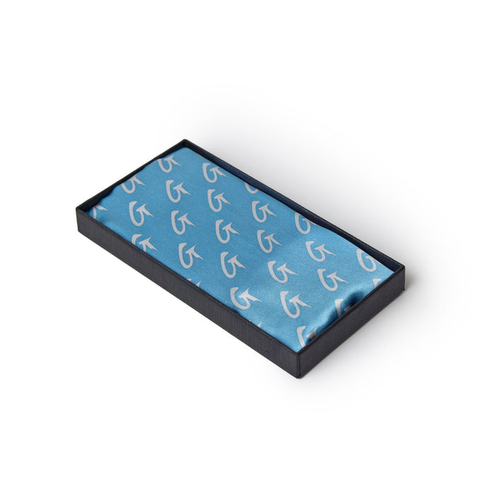 Medium silk scarf in blue and gold with a monogram pattern, presented in a black box with a matching blue interior.