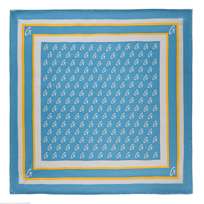 Medium blue silk scarf with a gold monogram pattern and border, featuring white "G" initials on a stylish design.