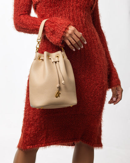 Medium pebble bucket bag in nude color with gold hardware, worn over a red textured sweater dress.
