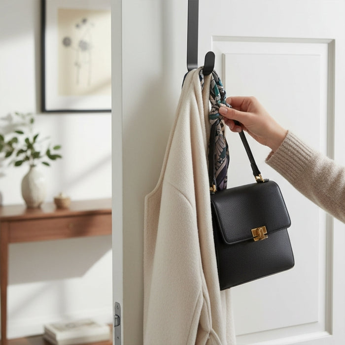 A person hanging a black handbag over a white coat and floral scarf on a metal wreath hook.
