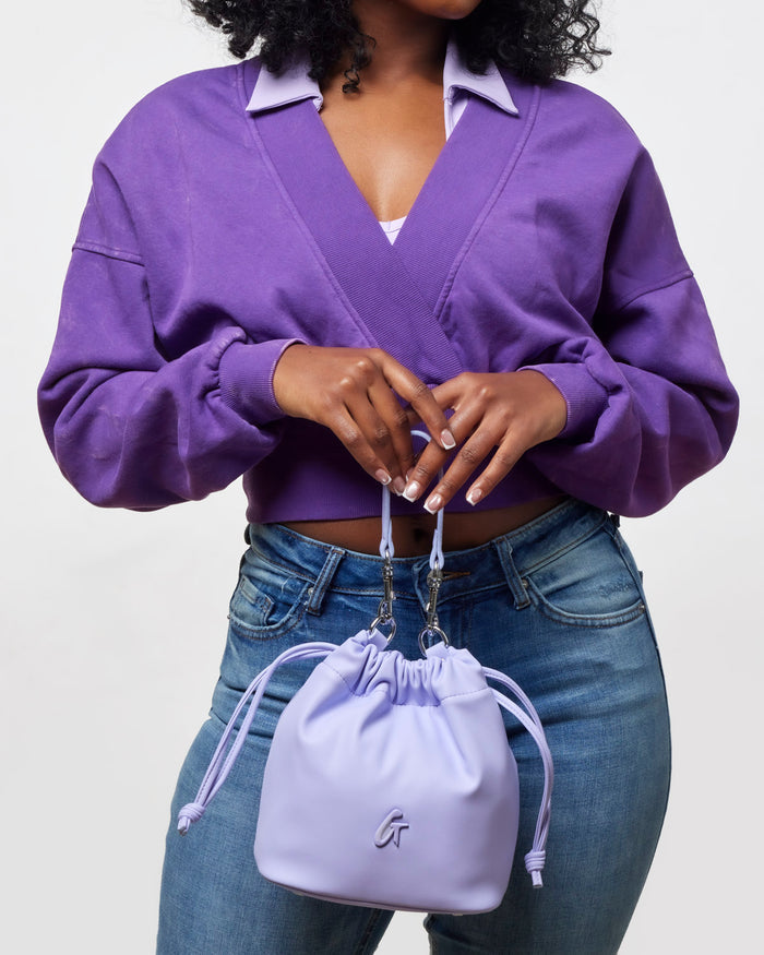Lavender mini drawstring bucket bag held by a model wearing a purple top and jeans, showcasing affordable luxury style.