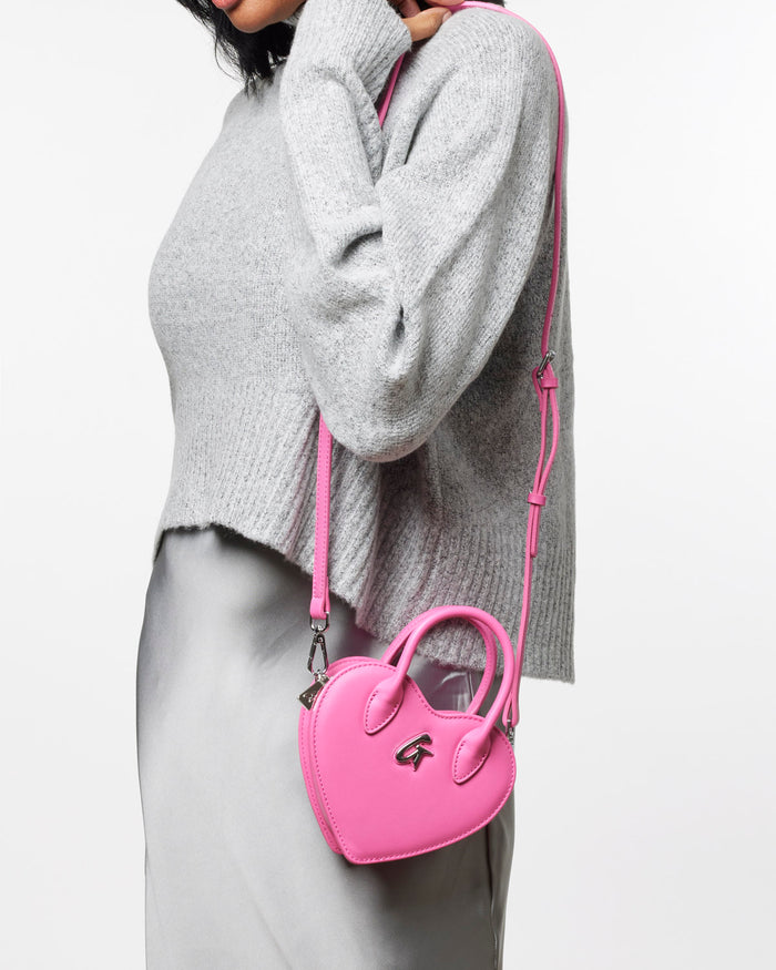 Mini heart-shaped pink handbag worn crossbody, featuring a sleek design and stylish handle, perfect for trendy outfits.
