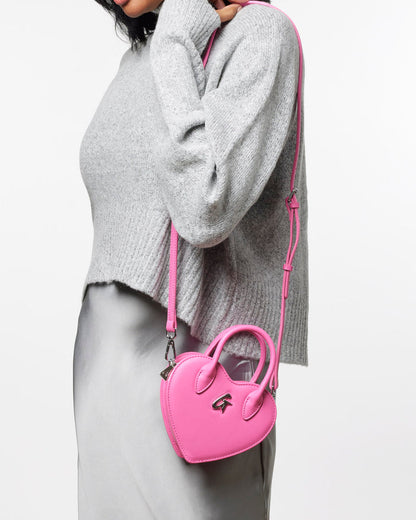 Mini heart-shaped pink handbag worn crossbody, featuring a sleek design and stylish handle, perfect for trendy outfits.