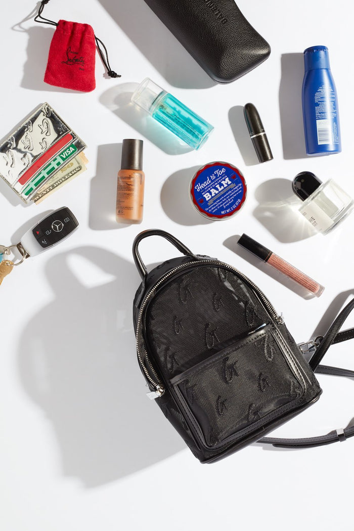 Mini mesh monogram backpack in black with a zipper closure, surrounded by small personal items on a white background.