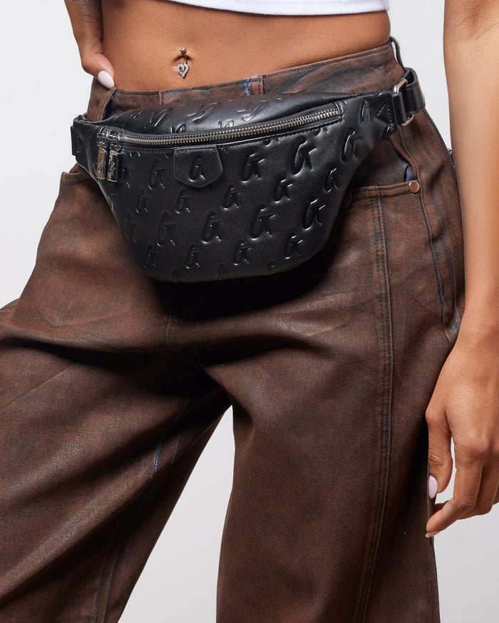 Black mini monogram fanny pack worn at the waist, featuring a zippered closure and embossed logo design.