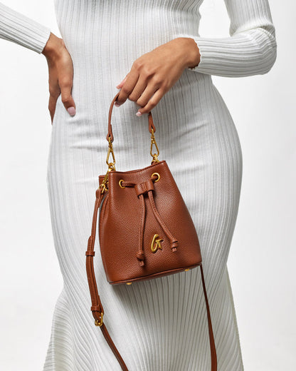 Mini pebble bucket bag in brown leather with gold hardware, featuring a drawstring closure and adjustable strap.