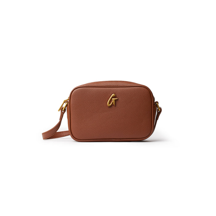 Brown mini pebble camera bag with a gold logo, adjustable strap, and textured leather finish.