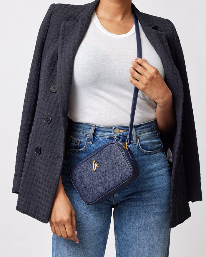Mini Pebble Camera Bag in navy, worn crossbody with a textured leather finish, featuring a gold logo on the front.