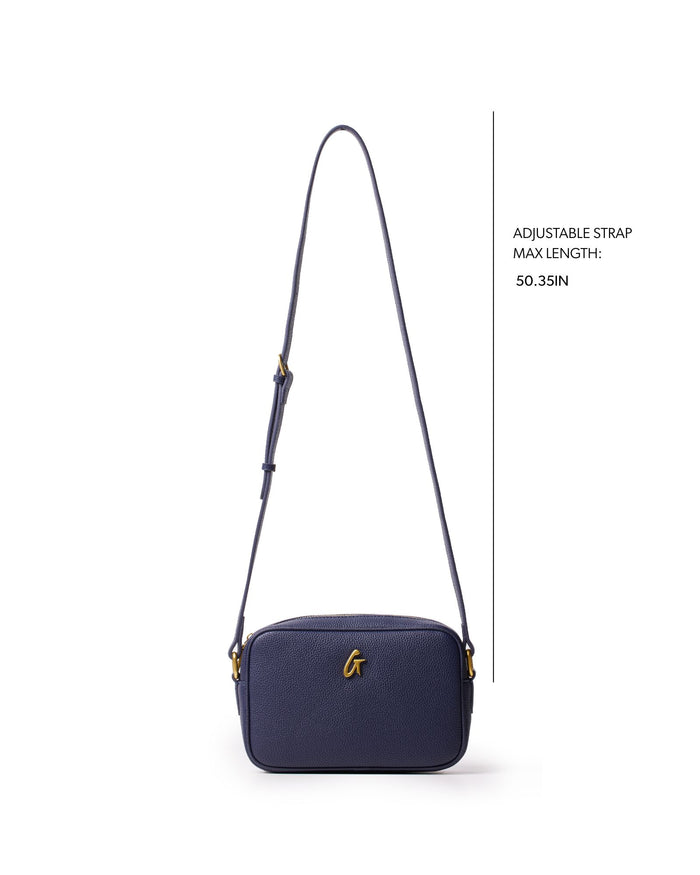 Navy mini pebble camera bag with adjustable strap, featuring a sleek design and gold logo detail.