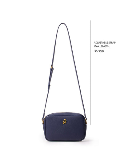 Navy mini pebble camera bag with adjustable strap, featuring a sleek design and gold logo detail.