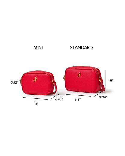 Mini pebble camera bag in red, featuring a sleek design and gold logo, with size comparison to standard bag.