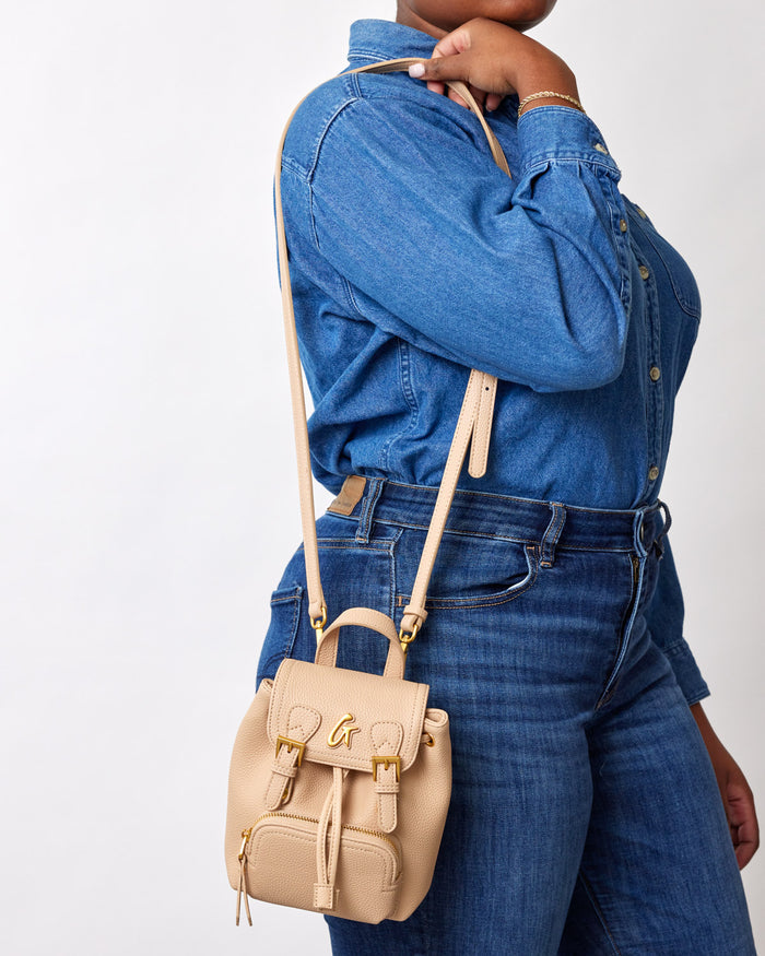 Mini Pebble Crossbody Backpack in nude color, worn over a denim outfit, featuring a small, textured leather design with gold hardware.