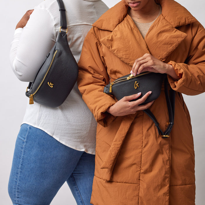 Two women display black Pebble Fanny Pack Bundles with gold accents, one worn crossbody and the other held in hands.
