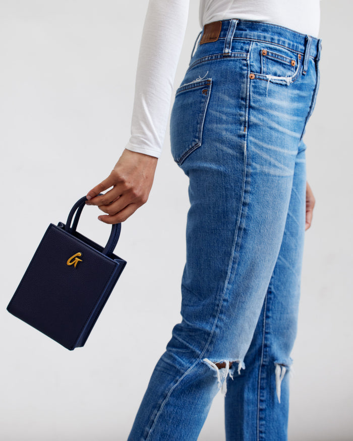 Mini Pebble Tote in navy blue, held by a person wearing ripped blue jeans and a white long-sleeve shirt.