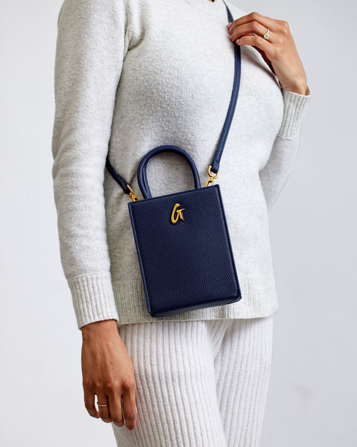 Mini Pebble Tote in navy with gold hardware, featuring a textured leather finish and a top handle, worn crossbody style.