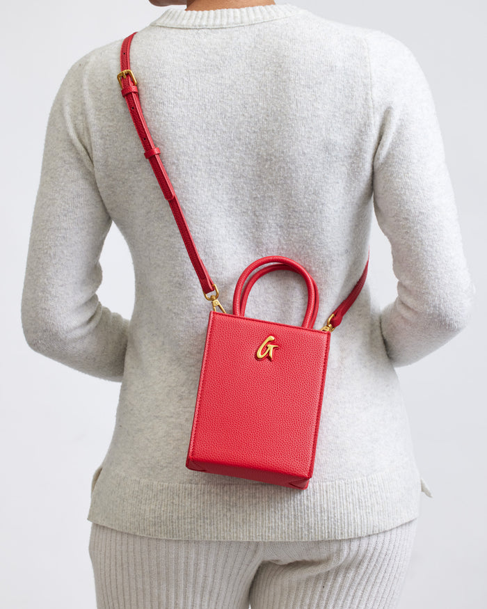 Red mini pebble tote bag with gold hardware, worn crossbody on a person in a light-colored sweater.