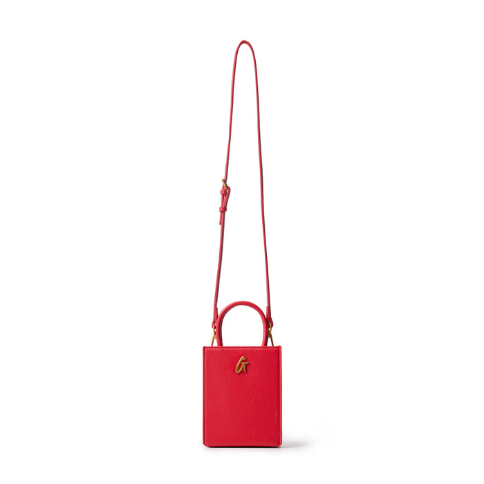 Red mini pebble leather tote bag with a top handle, gold logo detail, and adjustable shoulder strap on a white background.