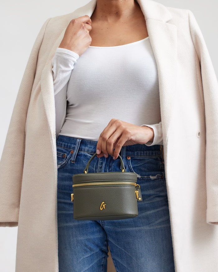 Mini pebble olive green vanity bag with gold accents, held by a woman in casual outfit, showcasing stylish compact design.
