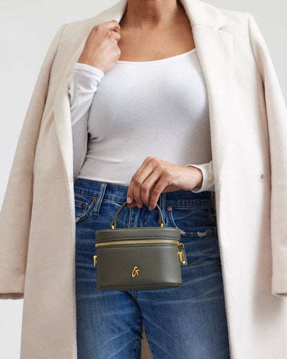 Mini pebble olive green vanity bag with gold accents, held by a woman in casual outfit, showcasing stylish compact design.