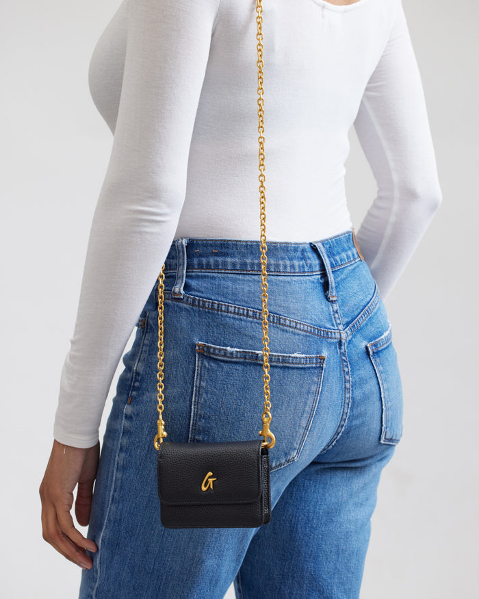 Mini Pebble WOC in black with a gold chain strap, worn over a white long-sleeve top and blue jeans.