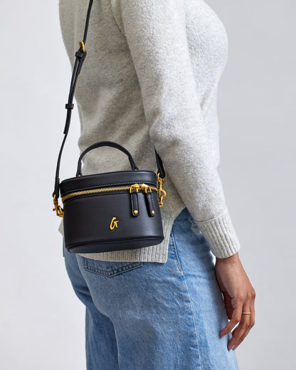 Mini black vanity bag with gold accents, top handle, adjustable strap, and a gold "G" logo.