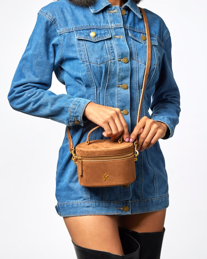 Mini suede vanity bag in brown, stylishly held by a model wearing a denim jacket, showcasing affordable luxury.
