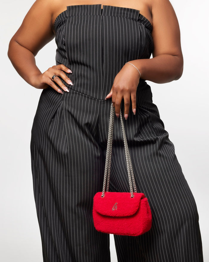 Mini Teddy Flap Bag in red held by a woman wearing a black striped jumpsuit, showcasing its stylish design.