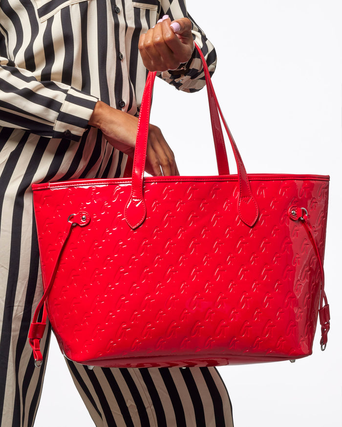 Shiny mirror red monogram tote bag held by a person in a striped outfit, showcasing its stylish design and spacious interior.