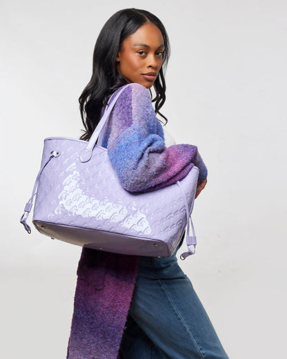 Monogram Glam Tote in mirror lavender, stylishly carried by a woman in a colorful sweater, showcasing affordable luxury.