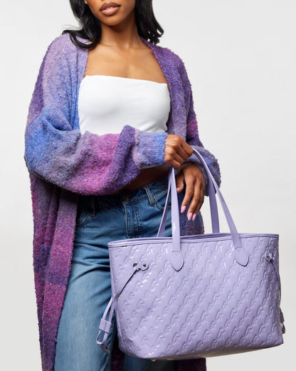 Lavender monogram tote bag with wristlet, featuring a glossy finish, stylishly held by a woman in casual attire.