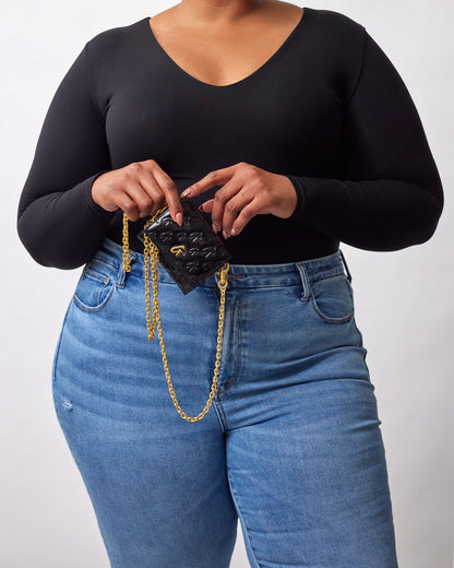 A woman holding a black compact mirror with a gold chain, featuring a monogram design and black mirror finish.