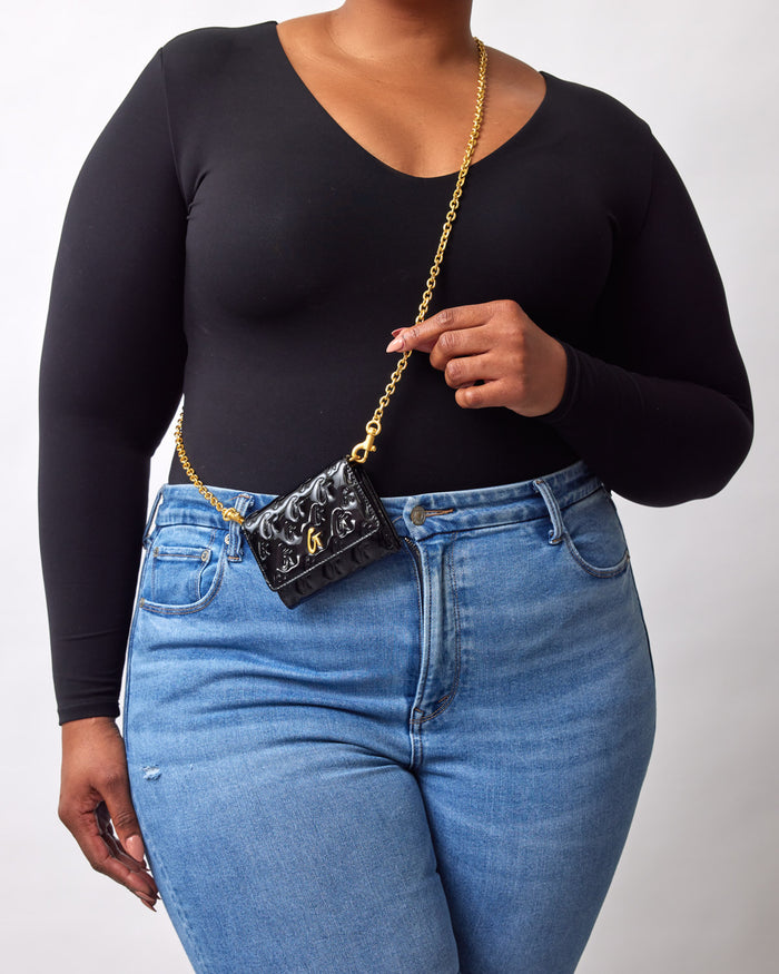 Mini black compact mirror with gold chain strap, featuring a monogram design and a reflective black surface.