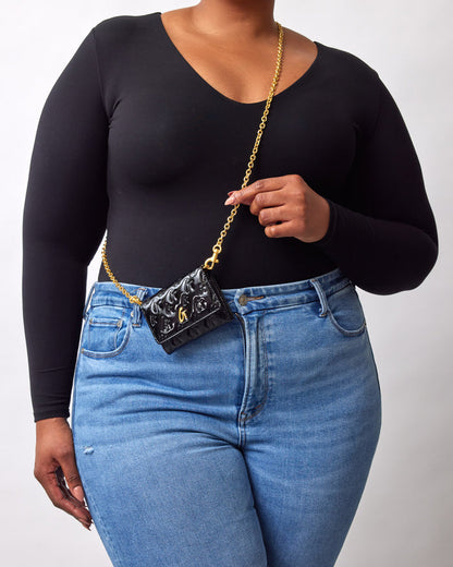 Mini black compact mirror with gold chain strap, featuring a monogram design and a reflective black surface.