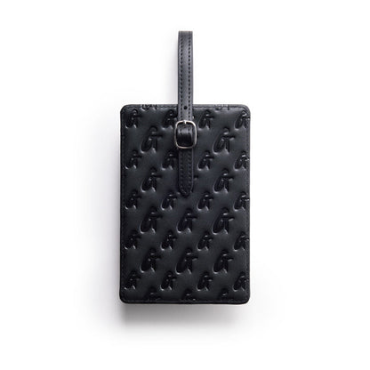 Black monogram luggage tag with embossed logo pattern and adjustable strap for secure attachment.