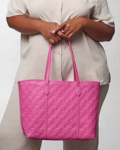 A woman holds a vibrant hot pink Monogram Sleek Tote with embossed logo pattern and matching handles.